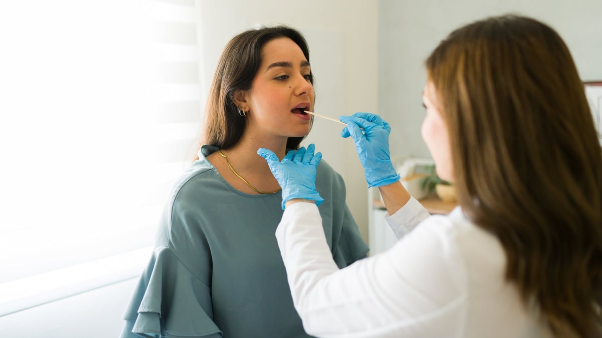 Female doctor in blue gloves swabs a patient's throat during a medical exam in a clinic. This image shows healthcare in action, emphasizing the importance of thorough checkups